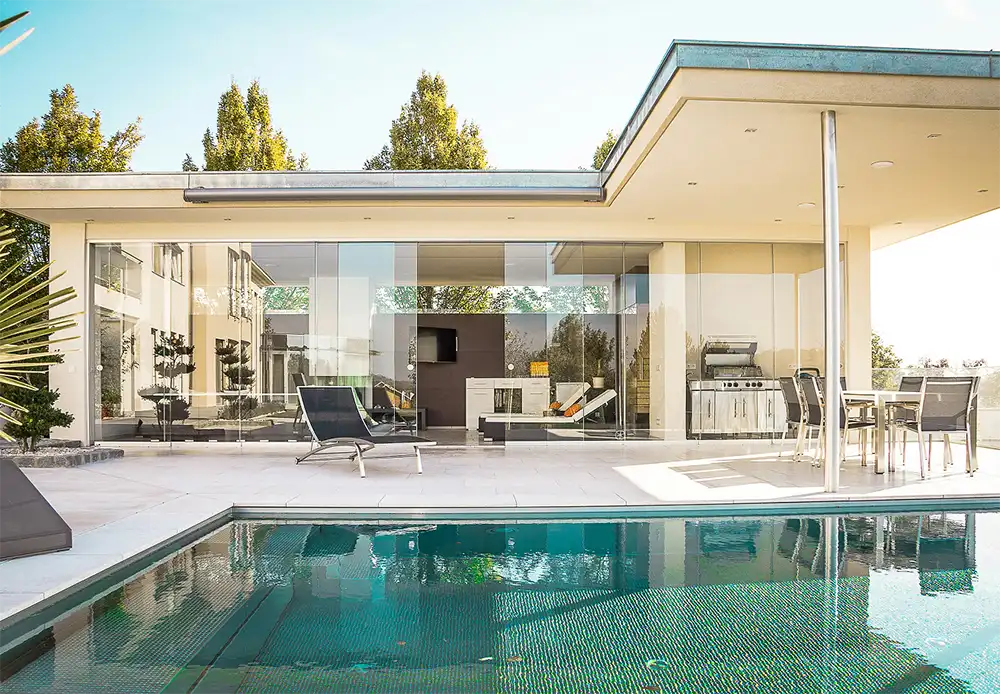 Modern luxury home with floor-to-ceiling glass walls and outdoor pool, representing high-end real estate investment opportunities.