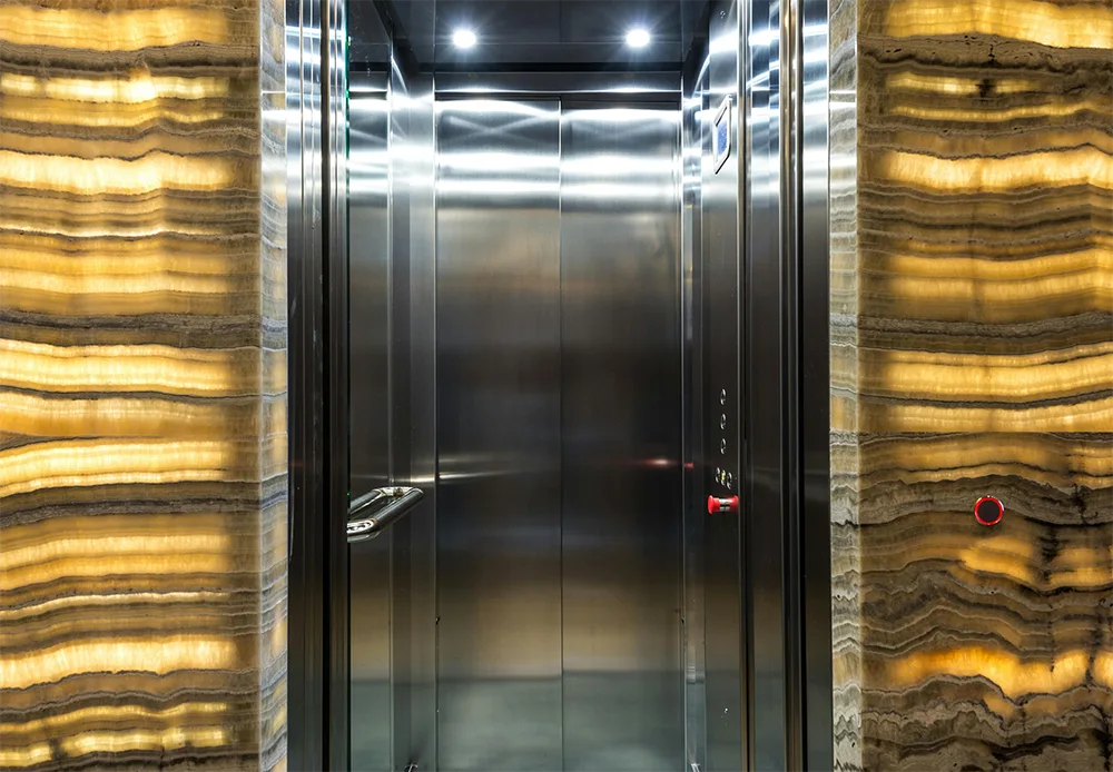 Open luxury elevator with polished metal doors and illuminated marble walls, symbolising upward movement and investment growth opportunities.