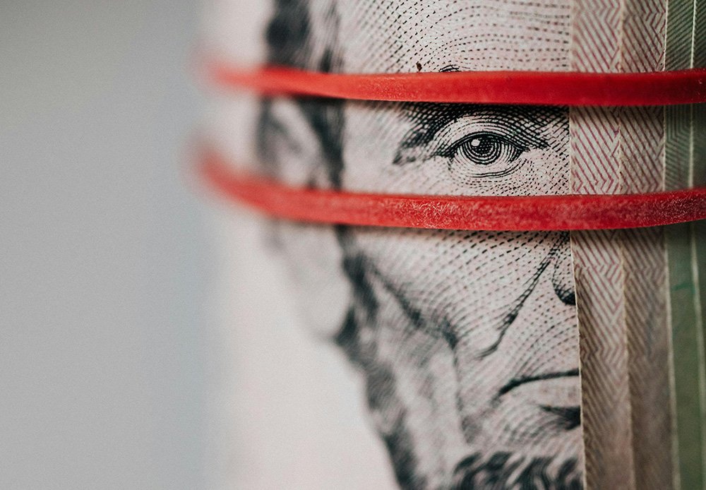 Close-up of rolled U.S. currency secured with red rubber bands, featuring a detailed view of Abraham Lincoln’s face from the five-dollar bill.