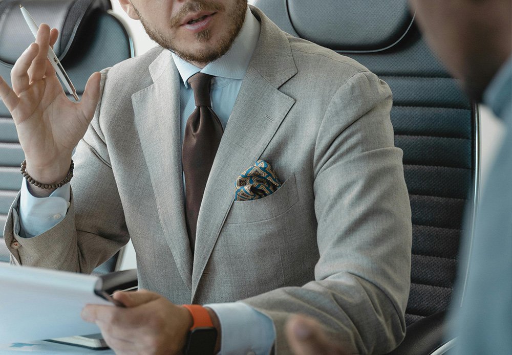Close-up of a business professional in a light grey suit and tie, gesturing with a pen during a meeting, symbolising strategic discussions in investment decision-making.