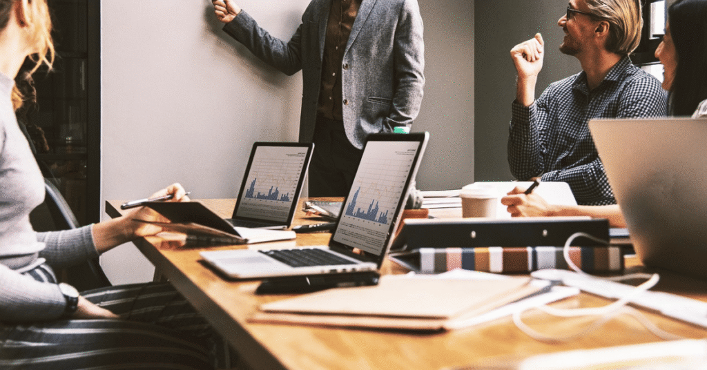 Team of professionals in a boardroom reviewing charts on laptops during an investment strategy meeting.