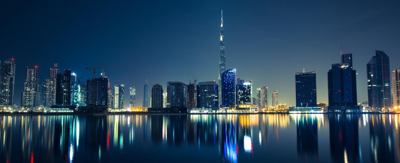 Dubai skyline at night with illuminated buildings reflected on water, symbolising global finance, international connectivity, and WIUS Capital’s presence in private markets.