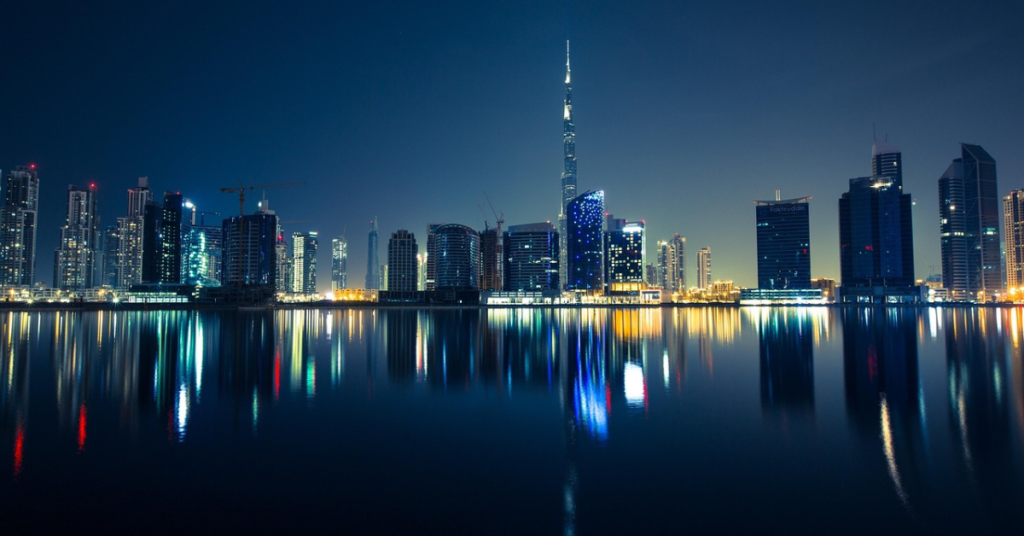 Dubai skyline at night with illuminated buildings reflected on water, symbolising global finance, international connectivity, and WIUS Capital’s presence in private markets.