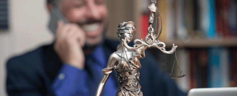 Lady Justice statue in foreground with a professional speaking on the phone in the background, illustrating legal case assessment and due diligence in litigation funding loan notes.